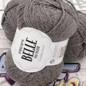 以下が含まれることがあります： 白ラベルが付いた、グレーの毛糸の3つの玉。「DROPS BELLE」と「Everyday Soft」と書かれています。糸はきつく巻かれており、柔らかく見えます。背景は、微妙なパターンを持つ明るい色の表面です。