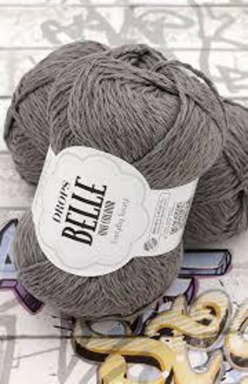 以下が含まれることがあります： 白ラベルが付いた、グレーの毛糸の3つの玉。「DROPS BELLE」と「Everyday Soft」と書かれています。糸はきつく巻かれており、柔らかく見えます。背景は、微妙なパターンを持つ明るい色の表面です。