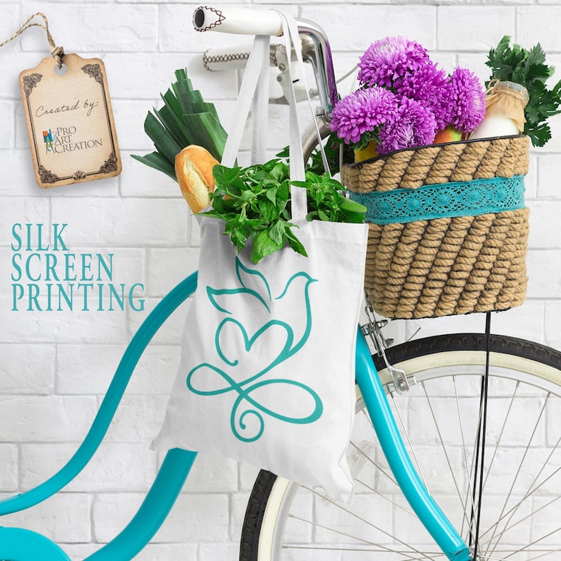 Peut inclure: Un sac fourre-tout blanc avec un motif de colombe et de c&oelig;ur turquoise, rempli de produits frais, est suspendu &agrave; un v&eacute;lo turquoise. Un panier tress&eacute; sur le guidon contient des fleurs violettes et une bouteille. Le texte "SILK SCREEN PRINTING" est visible.