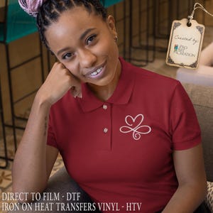 Puede incluir: Un polo granate con un dise&ntilde;o blanco en forma de coraz&oacute;n en el pecho izquierdo. La camisa tiene cuello y tres botones. El texto "DIRECT TO FILM - DTF IRON ON HEAT TRANSFERS VINYL - HTV" est&aacute; en la parte inferior de la imagen.