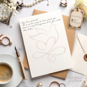 Peut inclure: Un ensemble de papeterie avec une carte cr&egrave;me orn&eacute;e d'un motif de colombe et de c&oelig;ur et d'un texte manuscrit. La carte est pos&eacute;e sur une enveloppe marron, avec une enveloppe blanche et une &eacute;tiquette "Cr&eacute;&eacute; par: Pro Art Creation". Un stylo, du caf&eacute; et des bijoux sont visibles.