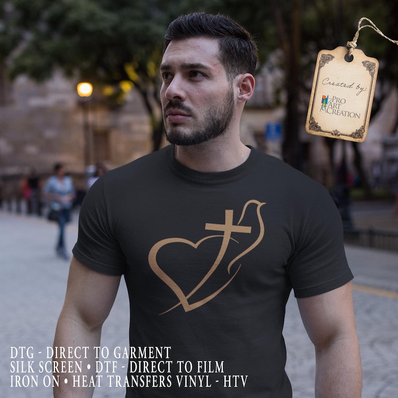 May include: Black t-shirt featuring a gold-colored graphic of a heart, cross, and dove. The shirt has short sleeves and is made of a soft material. The tag says "Created by: PRO ART CREATION".