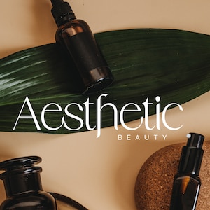 Op de afbeelding: Drie bruine glazen flessen met druppelaars en een kurkstop op een groen blad en een kurkoppervlak. De tekst "Aesthetic Beauty" is wit op een beige achtergrond.