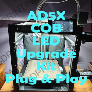 May include: A black 3D printer with a rectangular build plate and a digital display. The text "AD5X COB LED Upgrade Kit Plug & Play" is overlaid in blue. The Flashforge logo is visible.