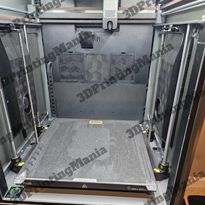 May include: A close-up view of the interior of a 3D printer. The printer has a black and gray build platform with a textured surface. The platform is labeled "CREALITY" and "350 x 350".