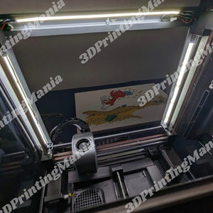 May include: A 3D printer with a white light strip on the top and a black light strip on the side. The printer is printing a colorful image. The image is of a cartoon character with a red hat and a yellow shirt. The printer is in a room with a white wall and a black floor.