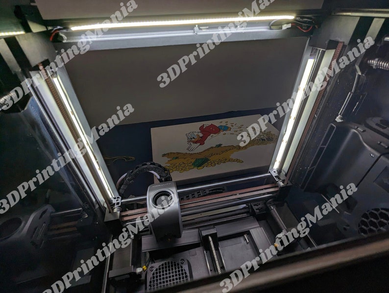May include: A 3D printer with a white light strip on the top and a black light strip on the side. The printer is printing a colorful image. The image is of a cartoon character with a red hat and a yellow shirt. The printer is in a room with a white wall and a black floor.