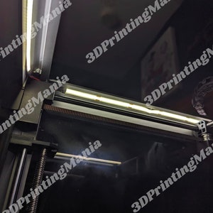 May include: A close-up of a 3D printer with two white LED light strips installed on the top. The light strips are illuminating the interior of the printer.