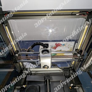 May include: A 3D printer with a clear plastic enclosure and a print bed. The printer is in the process of printing a multi-colored object. The print bed is lit by a strip of LED lights.