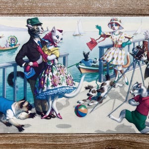 May include: A vintage postcard featuring a whimsical scene of cats dressed in clothing. A cat in a blue suit holds a cat in a floral dress. Another cat in a white dress and a cat in a red and white dress are also featured. The postcard has a nautical theme with a boat and a lighthouse in the background.