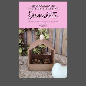 Könnte beinhalten: Ein hellbraunes, hausförmiges Vogelhaus mit einer weißen Keramik-Vogelfigur. Das Futterhaus enthält Vogelfutter und ist an einer weißen Schnur aufgehängt. Text auf rosa Hintergrund: "3D DRUCKDATEI IM STL & 3MF FORMAT Körnerhütte".