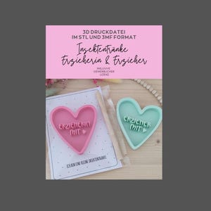Puede incluir: Un cortador de galletas en forma de corazón rosa y turquesa con las palabras "ERZIEHERIN MIT" y "ERZIEHER MIT" en relieve. La imagen también incluye una pancarta rosa con texto en alemán y una hoja impresa.