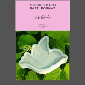May include: A light-coloured, bird-shaped 3D printed object, possibly a bird bath or feeder, set against a backdrop of green leaves. The image includes text in German: "3D Druckdatei im STL Format" and "Vogeltränke".