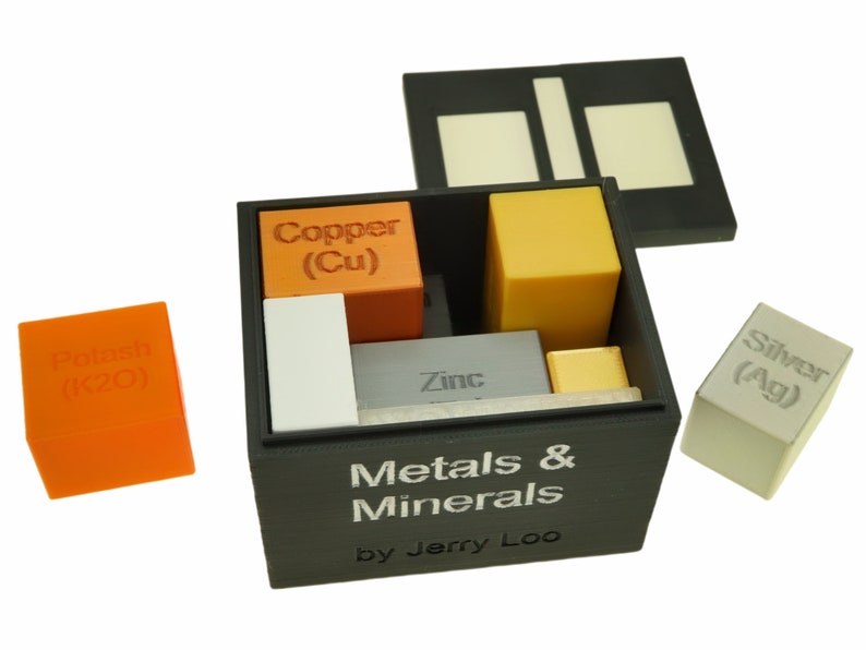 May include: A black box with a lid open, revealing a set of small cubes representing different metals and minerals. The cubes are labeled with their chemical symbols and names, including copper (Cu), zinc, silver (Ag), and potash (K20). The box is labeled "Metals & Minerals by Jerry Loo".