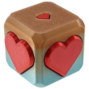 Könnte beinhalten: Ein würfelförmiges Fidget-Spielzeug mit einem Farbverlauf von Blau und Braun. Jede Seite des Würfels zeigt eine rote Herzform.