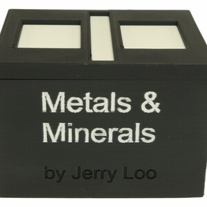 May include: A black wooden box with a white label that reads "Metals & Minerals by Jerry Loo". The box has two rectangular cutouts on the top.