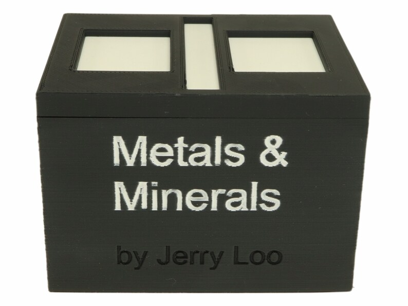 May include: A black wooden box with a white label that reads "Metals & Minerals by Jerry Loo". The box has two rectangular cutouts on the top.