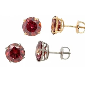 May include: A pair of stud earrings with round, red gemstones set in gold and silver settings. The earrings have a post and butterfly back.