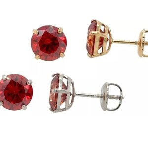 May include: A pair of red gemstone stud earrings with gold and silver settings. The earrings have a screw-back closure.
