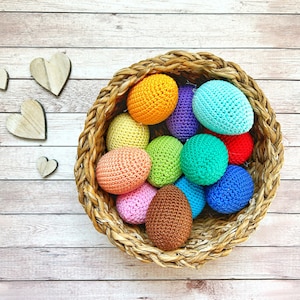 May include: A wicker basket filled with colourful crocheted Easter eggs. The eggs are in shades of green, blue, purple, pink, yellow, orange, and brown.