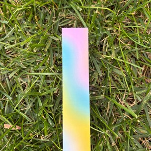 One gradient bookmark sitting on grass. Shows the different colors of the light blue, pink and yellow.