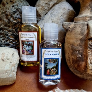 May include: Two small bottles, one containing clear liquid and the other containing yellow liquid. Both bottles have labels with religious imagery and text. The label on the clear bottle reads "Holy Water From The Blessed Jordan River" and the label on the yellow bottle reads "Anointing Oil Nard". Both bottles are made in the Holy Land.