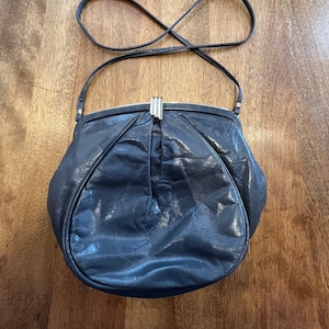 May include: A dark blue leather handbag with a silver clasp and a long strap. The bag is slightly wrinkled and has a rounded shape.