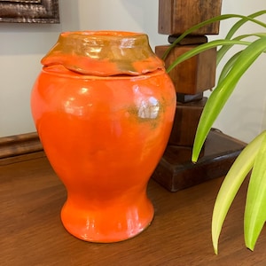 May include: Orange ceramic vase with a textured, glazed finish. The vase has a wide mouth and a rounded base.