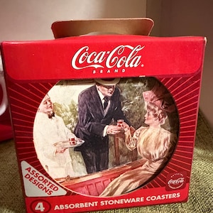 Puede incluir: Una caja roja de la marca Coca-Cola que contiene cuatro posavasos absorbentes de gres. La caja presenta una ilustración vintage de personas disfrutando de una bebida. Los posavasos tienen diseños variados.