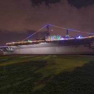 May include: A large, white ship decorated with colourful lights. The ship is docked at a pier and is surrounded by water. The ship is lit up with Christmas lights.