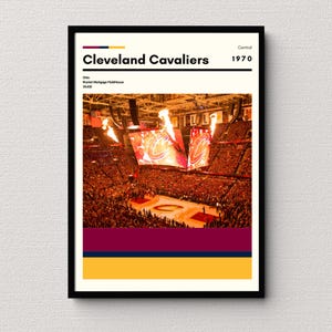 May include: A poster with a black frame featuring a photo of a basketball arena with a crowd of people. The poster has the text "Cleveland Cavaliers" and "1970" in black text on a white background. The poster also has the text "Ohio" and "Rocket Mortgage FieldHouse" in black text on a white background. The poster has a red, navy blue, and yellow color scheme.
