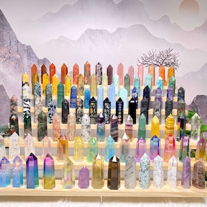 Pode incluir: Uma coleção de pontas de cristal coloridas dispostas em um suporte de madeira. Os cristais são de várias formas e tamanhos, e todos são polidos para um acabamento liso. O suporte é feito de madeira natural e tem um design simples.