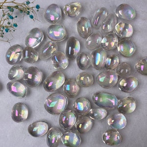 May include: A selection of clear, iridescent tumbled stones with a rainbow sheen. The stones are of various sizes and shapes, with a smooth, polished texture. A sprig of dried blue flowers is in the upper left corner.