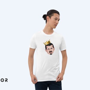 May include: White t-shirt with a cartoon illustration of a man wearing a gold crown. The man has a mustache and a beard.