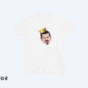 May include: White t-shirt with a cartoon illustration of a man wearing a gold crown.