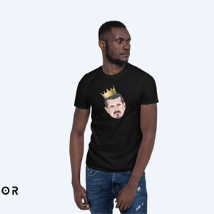 May include: A black t-shirt with a graphic of a man wearing a gold crown. The man has a mustache and beard.