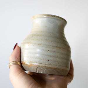 May include: A small, white ceramic vase with a brown glaze and a hand-stamped mark on the bottom.