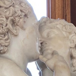 May include: A close-up of two white marble sculptures of people kissing. The sculptures are detailed and realistic, with the man's hair sculpted in a curly style.