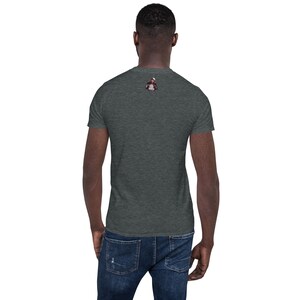 Puede incluir: Una camiseta gris oscuro jaspeada con un peque&ntilde;o gr&aacute;fico de una persona con un sombrero y una chaqueta en la espalda.