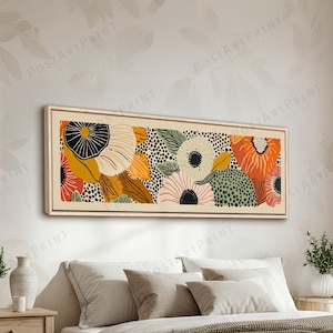 Op de afbeelding: Een ingelijste kunstdruk met een bloemmotief in oranje, geel, zwart en groen. Het kunstwerk hangt boven een bed met neutrale beddengoed, wat een rustgevende slaapkameromgeving creëert. De afmetingen van de print zijn geschikt voor een modern interieur.