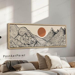 Puede incluir: Una impresión artística enmarcada que representa un paisaje de montañas y un sol en tonos beige, negro y naranja. La obra de arte se exhibe sobre un sofá seccional beige en un salón moderno. El texto "POSTARTPRINT ORIGINAL MODERN ART" es visible.