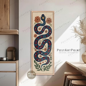 Op de afbeelding: Een verticaal ingelijste kunstprint met een gestileerd slangenontwerp in marineblauw met rode hartvormige accenten. Het kunstwerk bevat bloemen- en bladelementen tegen een lichtbeige achtergrond. Met de tekst "READY TO HANG" en "PostArtPrint".