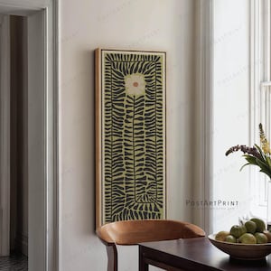 Peut inclure: Une impression d'art verticale encadrée avec un motif floral. Elle présente une fleur centrale et un motif de formes noires en forme de feuilles sur un fond vert clair. L'œuvre est accrochée à un mur de couleur neutre dans une salle à manger.