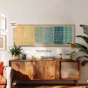 Könnte beinhalten: Ein langes, rechteckiges gerahmtes Wandkunstbild mit einem horizontalen Muster aus vertikalen Pinselstrichen in Orange-, Gelb-, Blaugrün- und Dunkelblautönen. Das Kunstwerk befindet sich in einem hellen Holzrahmen und enthält den Text PostArtPrint.