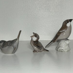 May include: Three ceramic bird figurines in shades of gray and brown. One bird is perched on a small, textured base. Another is in a singing pose, and the third is in a resting position.