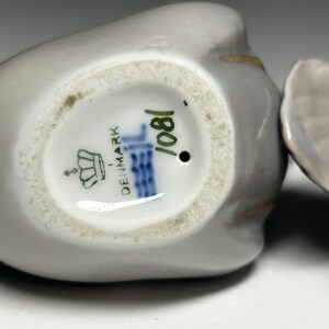 May include: Close-up of a porcelain figurine, likely a bird, with a gray and white color scheme. The base of the figurine is visible, displaying the text "DENMARK" and the number "1081". The figurine has a glossy finish.
