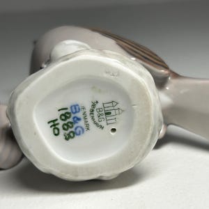 May include: A pair of ceramic bird figurines in shades of gray and brown. The underside of one bird shows the B&G Copenhagen Denmark mark, along with the numbers 1883 and HO in green ink. The birds are likely decorative items.