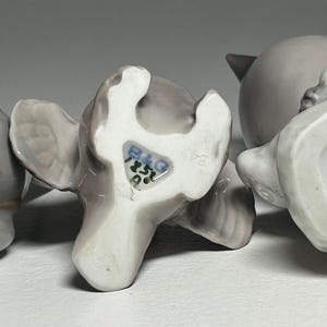 May include: Three ceramic bird figurines in shades of gray, with visible markings on the underside. The figurines are in various poses, showcasing their detailed craftsmanship. The bases display maker's marks and numbers, indicating their origin and design.