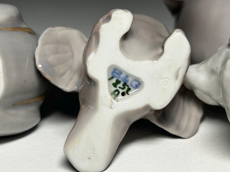 May include: Close-up of a collection of porcelain elephant figurines in various poses. The elephants are primarily gray with white accents and feature the B&G mark on the underside. The figurines are likely vintage or antique.