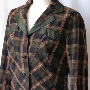 May include: A tailored blazer in a brown, green, and red plaid pattern. The jacket has a notched collar and green trim on the pockets. It is fastened with three brown buttons and displayed on a mannequin.